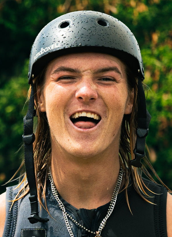 Daniel J team headshot with a huge smile and wearing a black helmet with trees in the background.