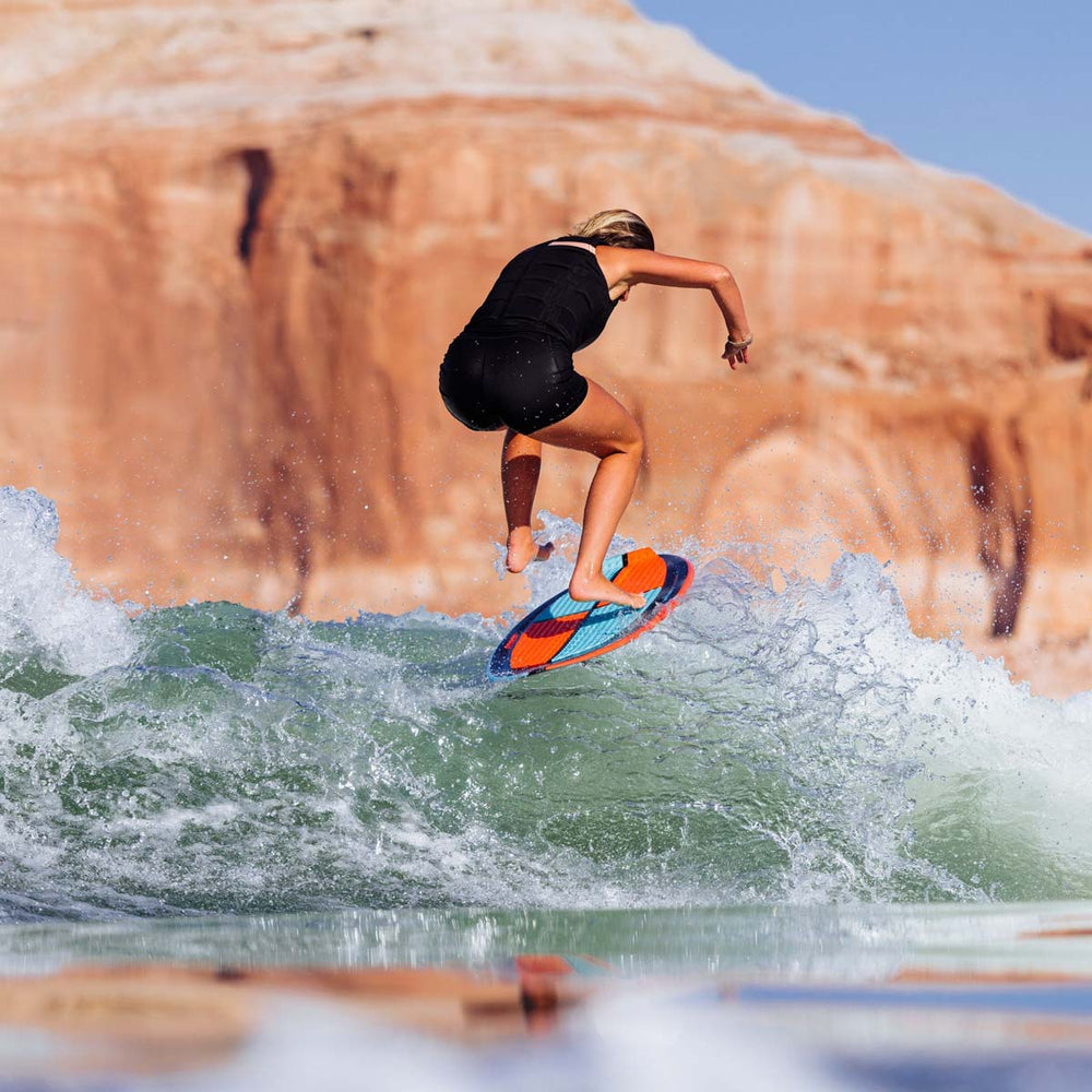 Bailey D surfing on a blue and orange colorful board with a rock formation in the background