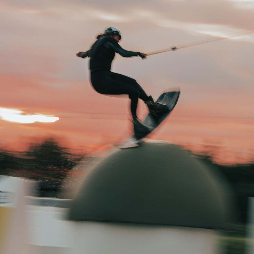 Sanne M wakeboarding at sunset with a blurred background jumping off a large sphere in the water