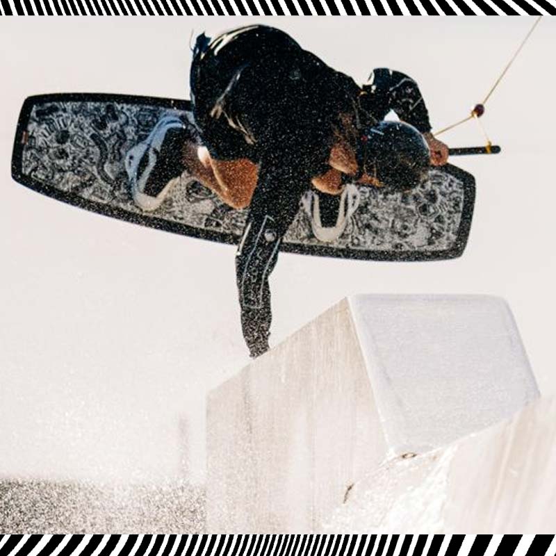Wakeboarder in mid-air performing a rail trick with a black patterned board.