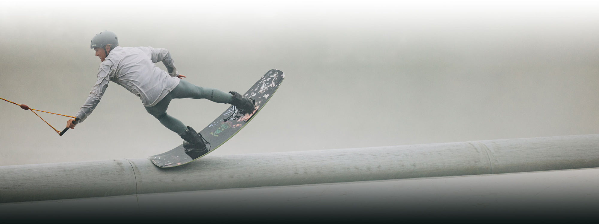 Wakeboarder with a helmet, gripping the rope on a misty day.