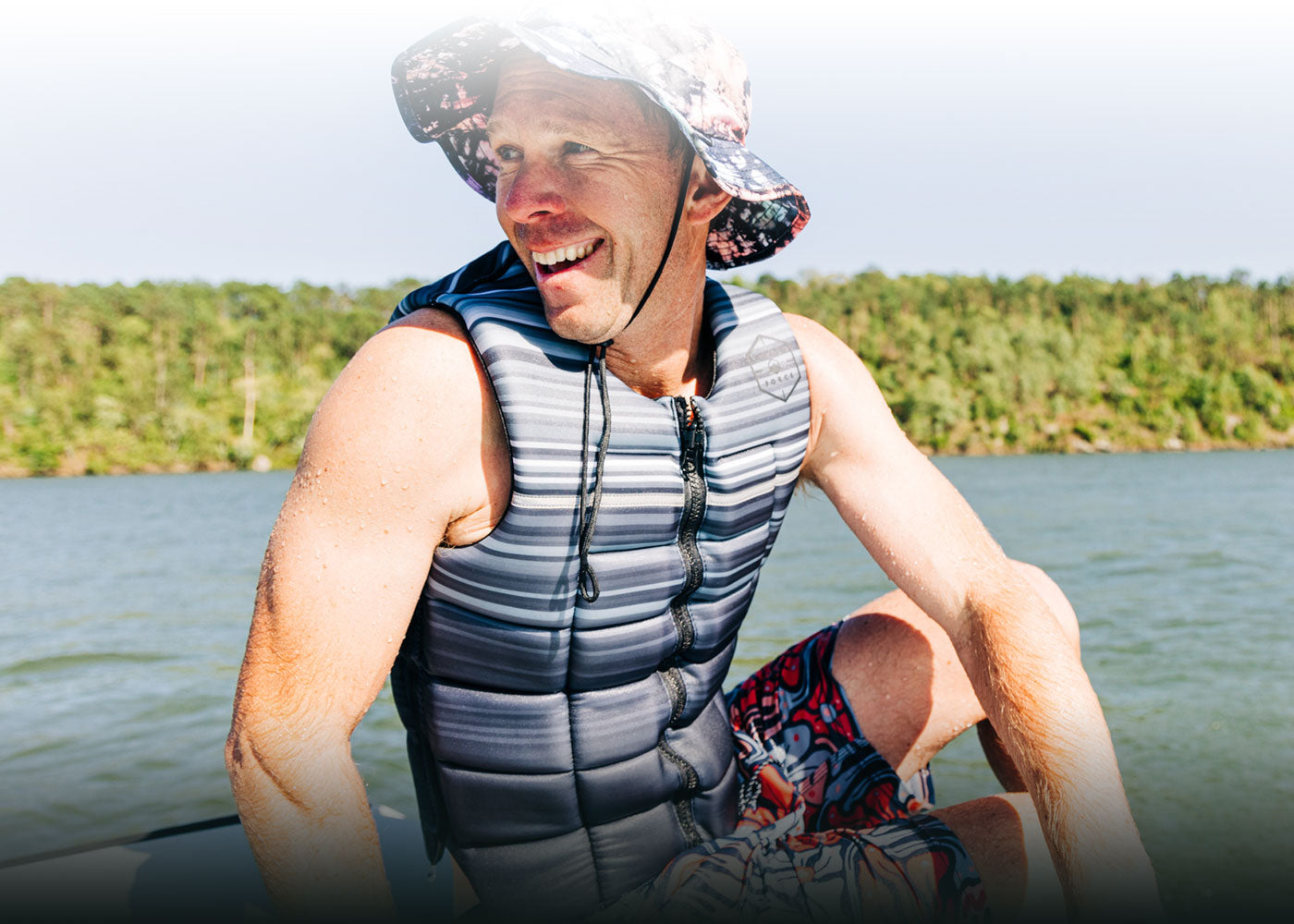 Person in a hat and life vest grinning on a sunny boat trip.