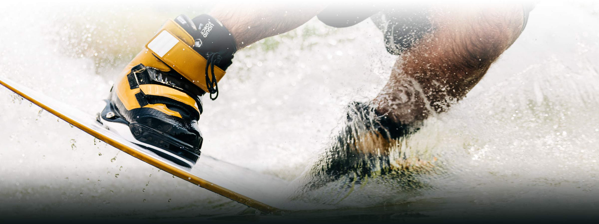 Close-up of a person wakeboarding, water splashing, wearing yellow and black boots while surfing.