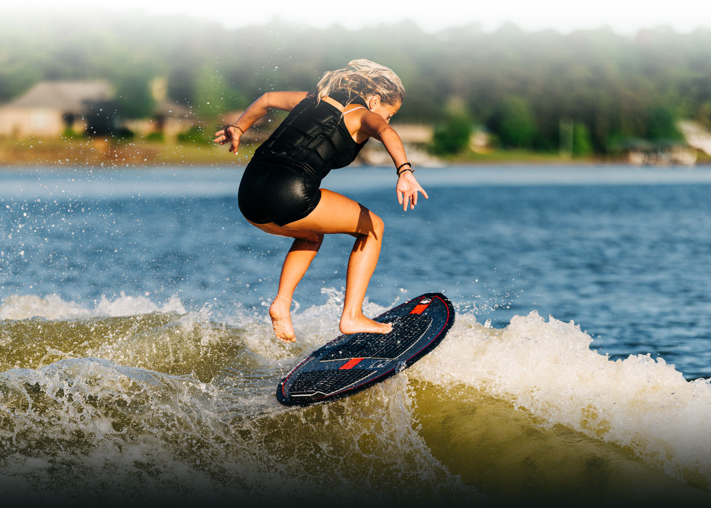 Person riding waves on a black board near a tranquil lake.