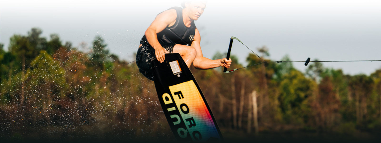 Wakeboarder soaring mid-air amidst lush trees.