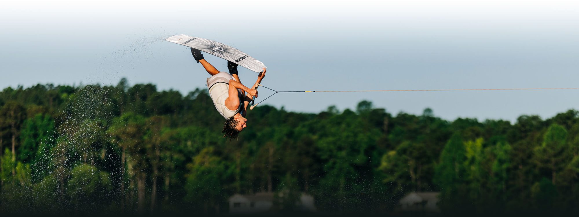 Wakeboarder flipping through the air with trees and sky all around.