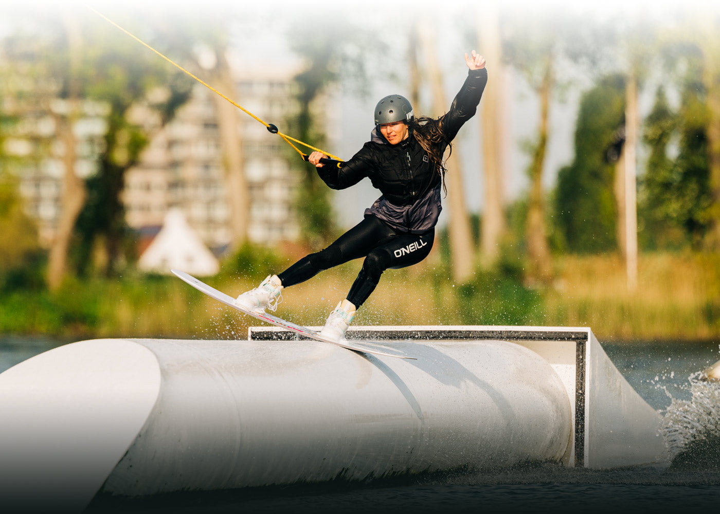 Wakeboarder gliding on a rail in a lake, donning helmet and wetsuit.