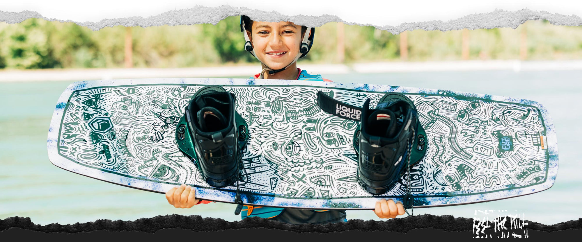 Smiling child holds a Liquid Force APEX FS wakeboard with black boots and a doodle-style design.