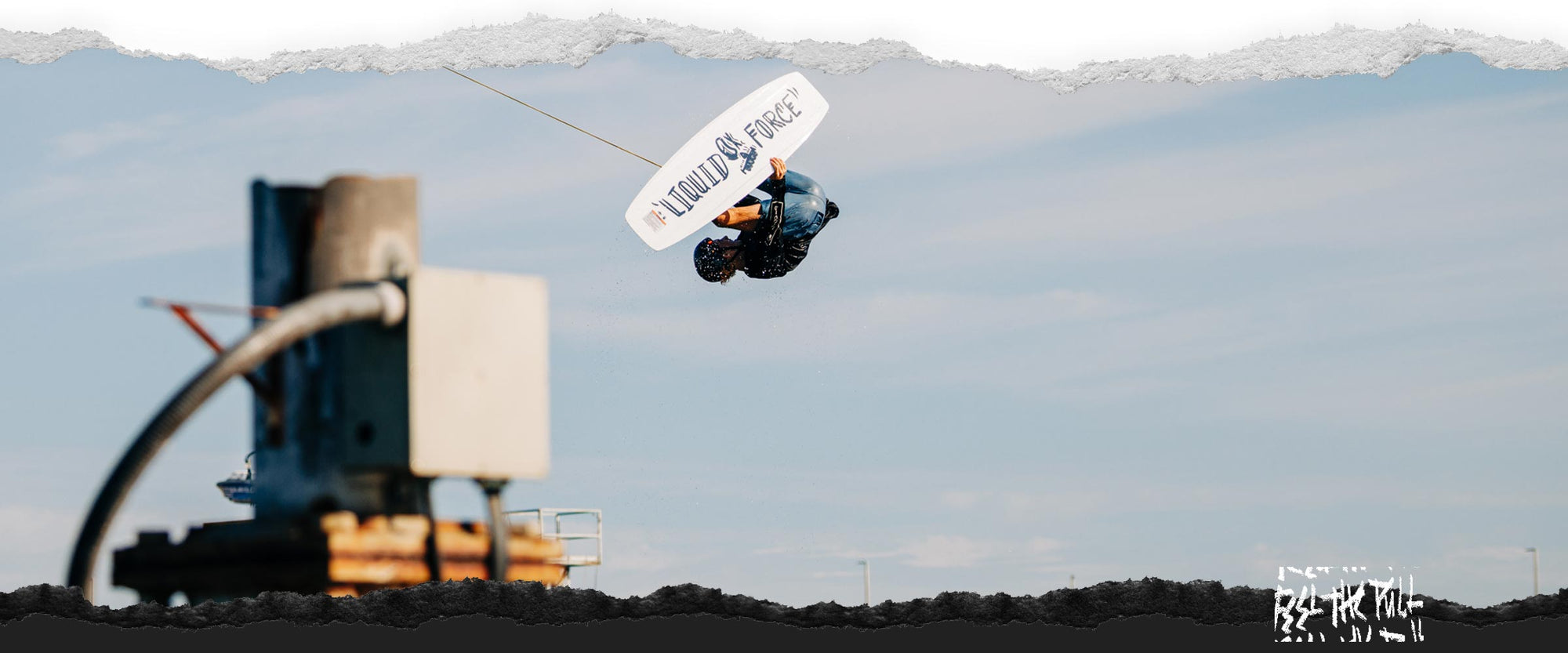 Wakeboarder performing a jump in the air with the wakeboard and rope visible.