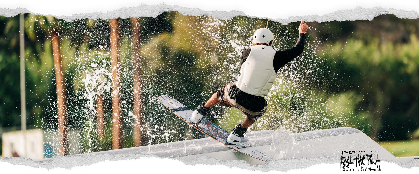 Rider wakeboarding in white vest, hitting a rail with water spraying behind.