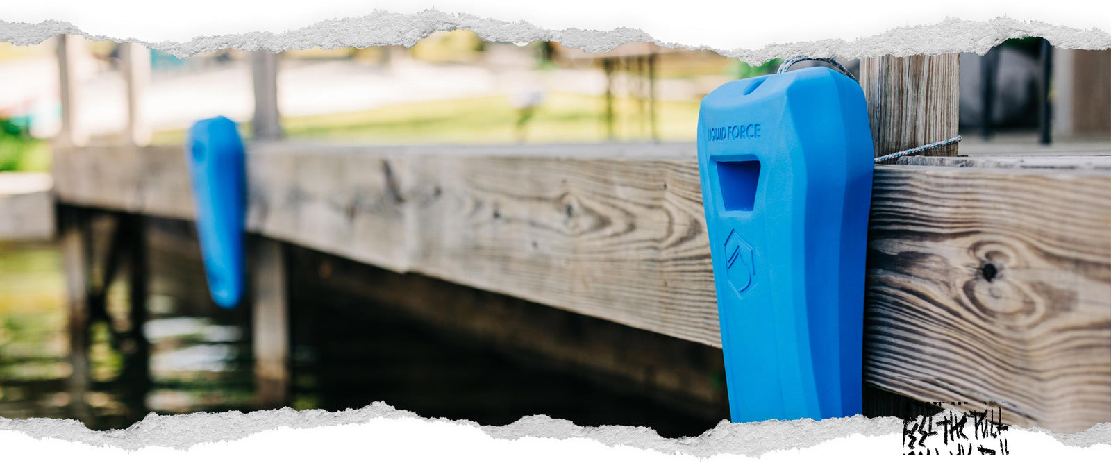 Blue Liquid Force boat defender tied to wooden dock next to water.