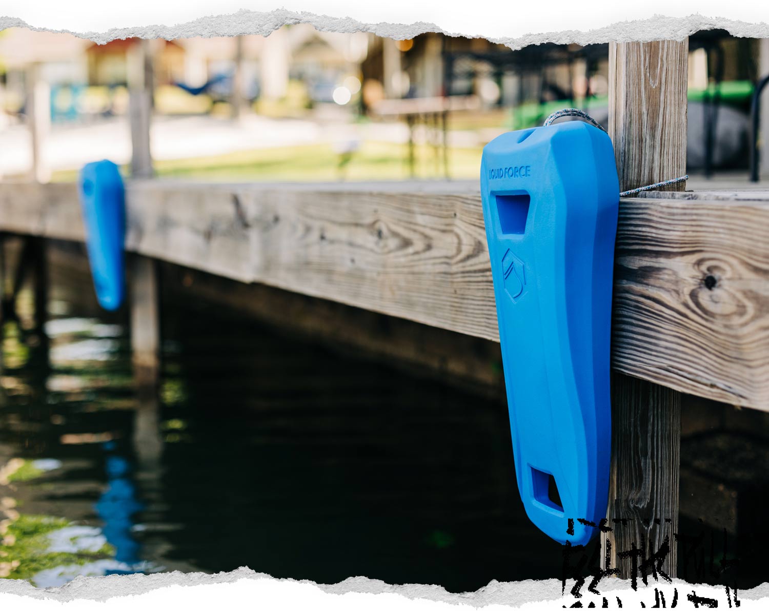 Blue Liquid Force boat defender tied to wooden dock next to water.