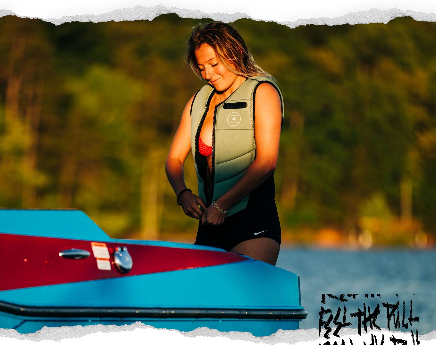 Woman zips green Breeze Comp vest at sunset beside a blue and red boat.