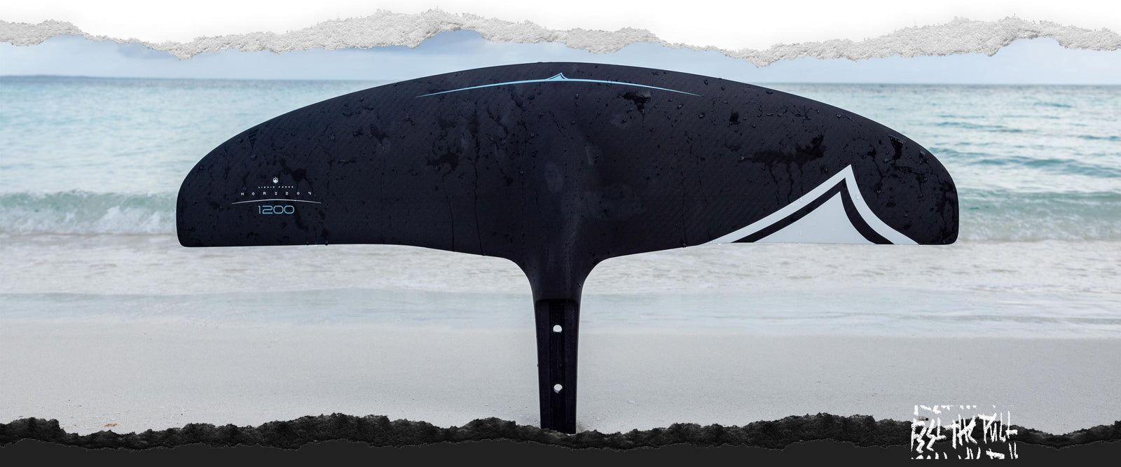 Black Horizon 1200 foil wing stands upright on wet sand near shoreline.