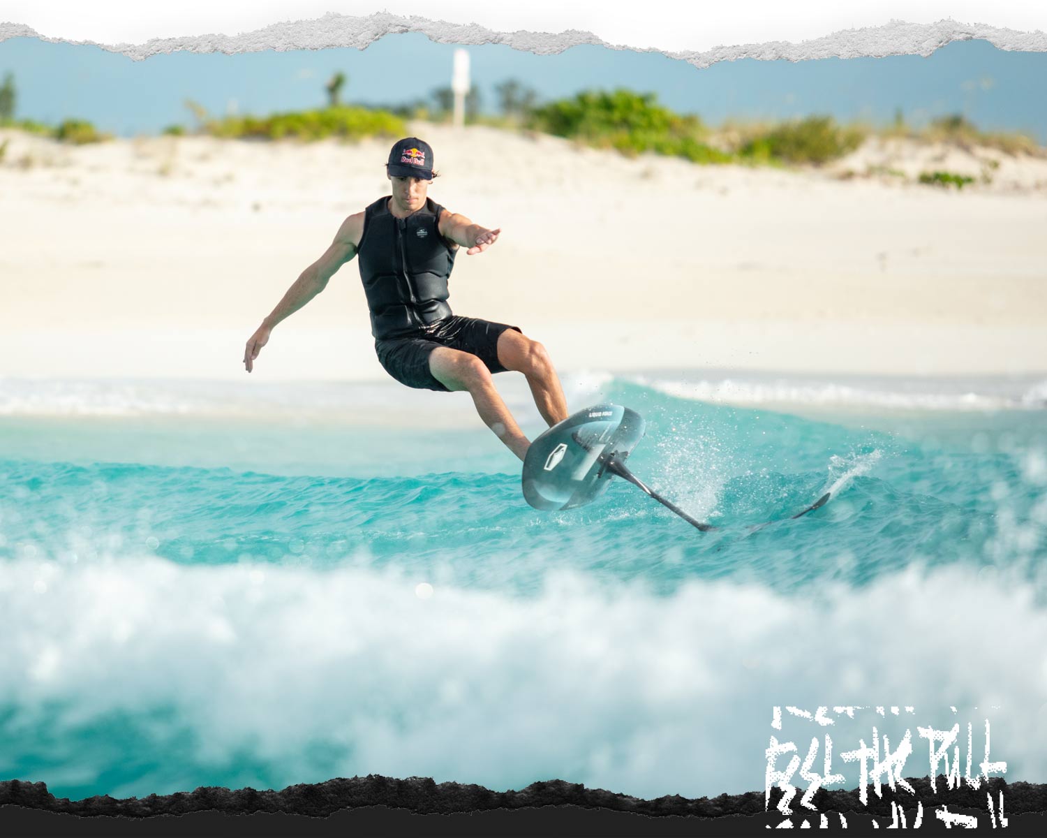 Man in black vest and Red Bull hat balances on a foil board near the beach.