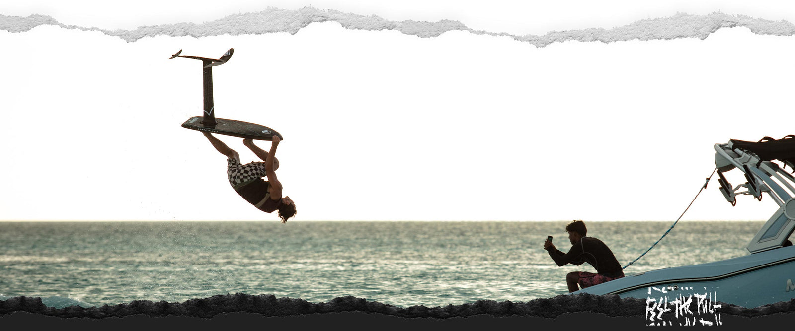 Foil boarder does a sunset flip while a man records from the back of a boat.