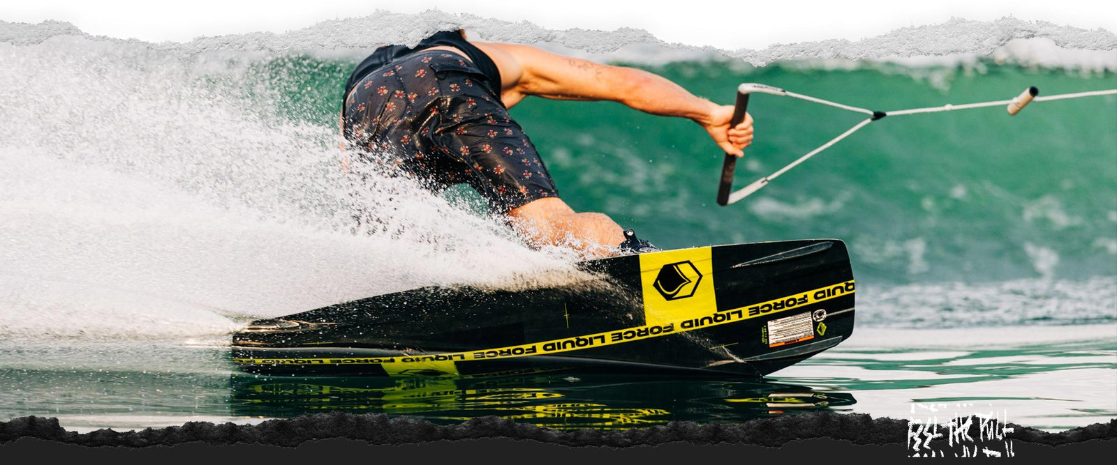 Wakeboarder in floral shorts carves hard turn on black and yellow Liquid Force board.