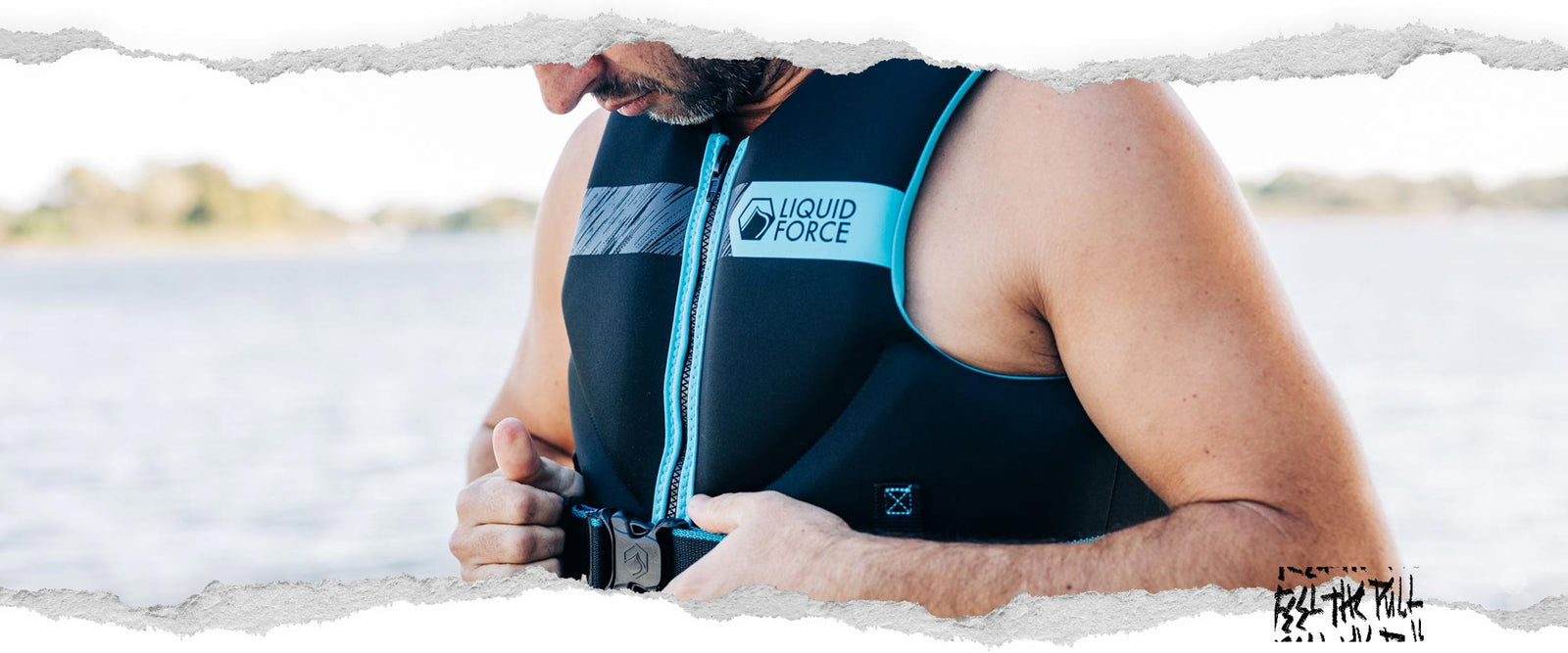 Hombre ajustándose el chaleco negro y azul Classic Hinge CGA con el logotipo de Liquid Force en la orilla del lago.