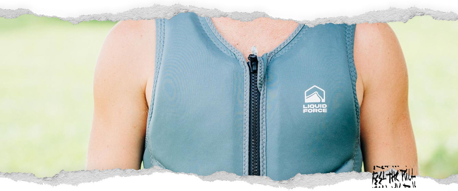 Man in grey Core Comp vest stands outdoors in grass with trees in background.