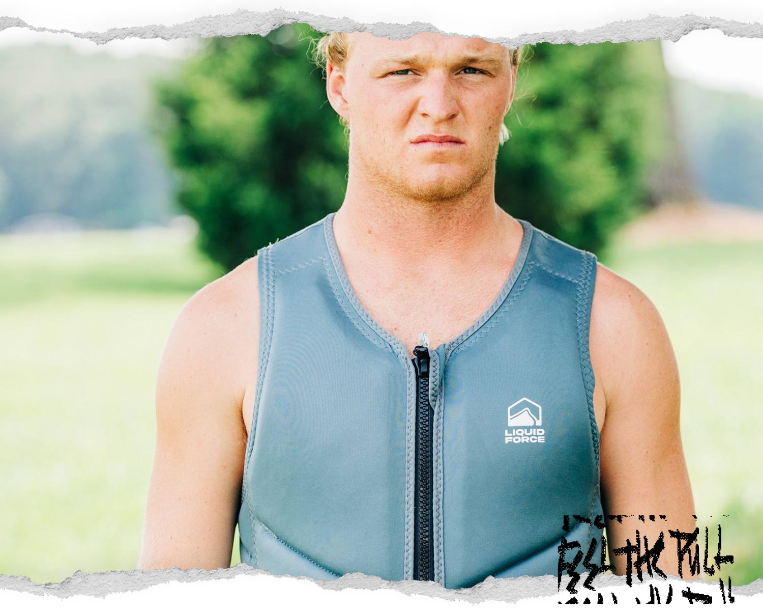 Man in grey Core Comp vest stands outdoors in grass with trees in background.