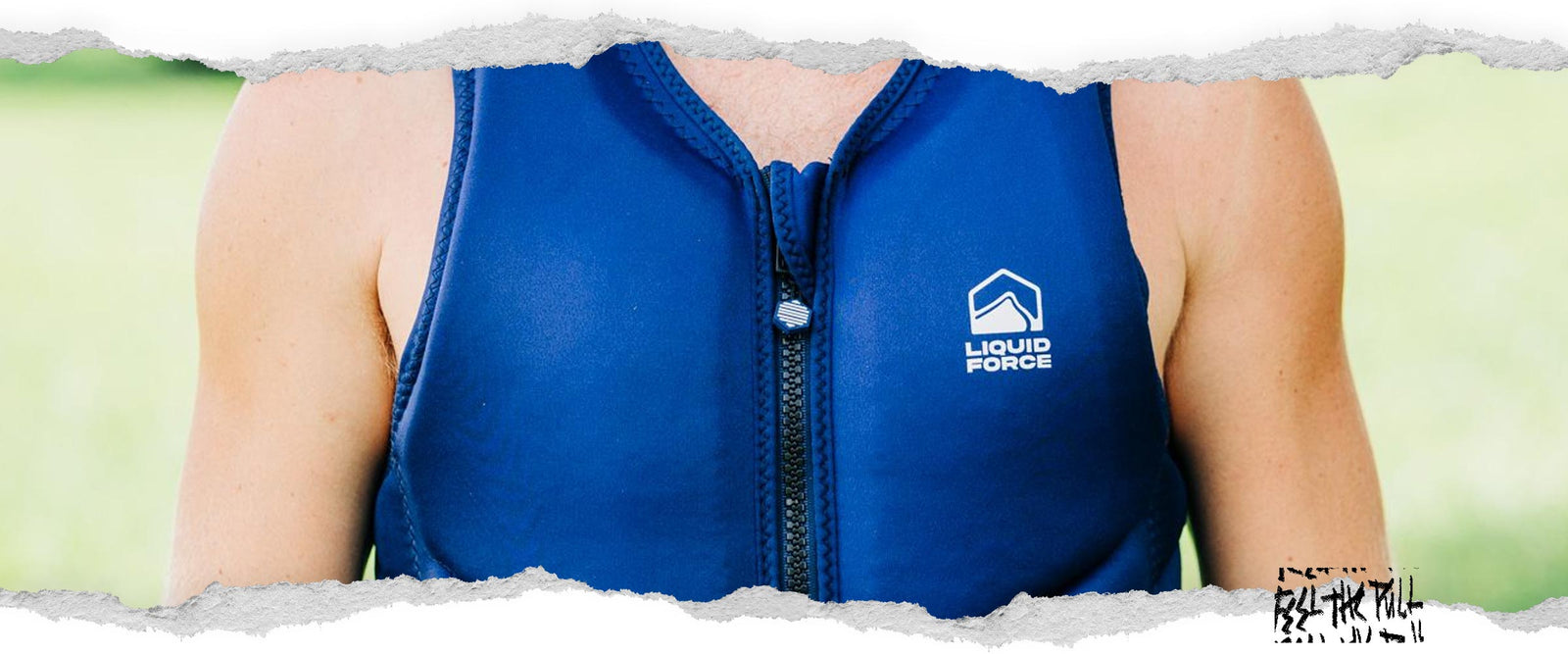 Un hombre con un chaleco azul marino Core Comp se encuentra al aire libre en el césped con árboles de fondo.