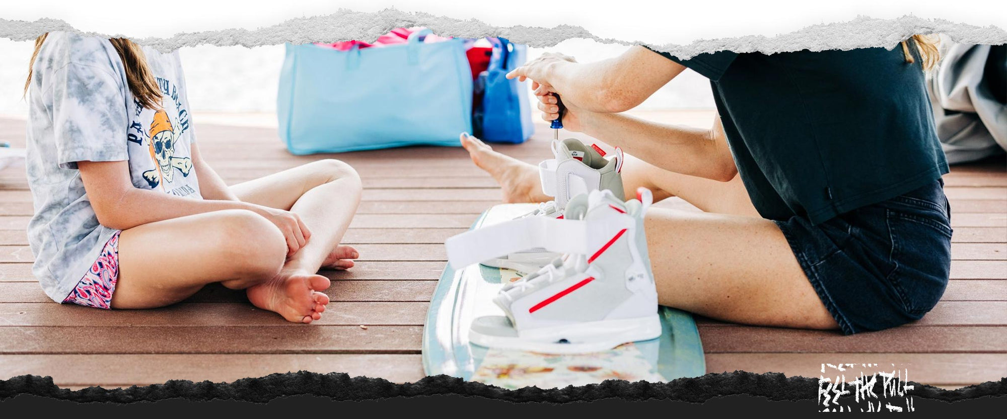 Woman adjusting white and red bindings on dock beside seated child.