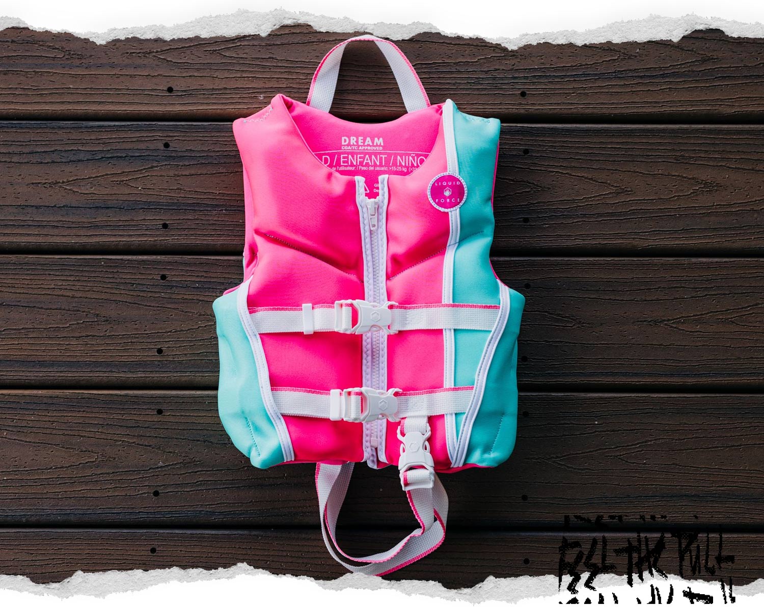 Front view of pink and mint Liquid Force child CGA vest with white straps on dark wood deck.