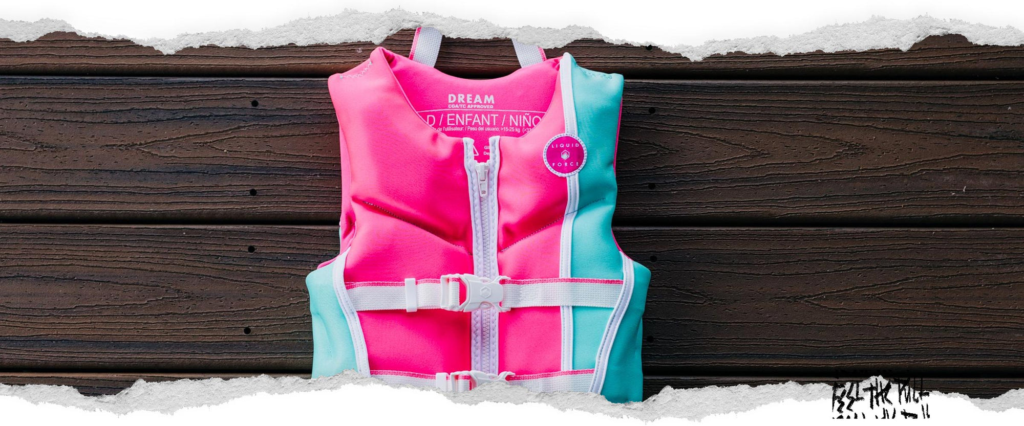 Front view of pink and mint Liquid Force child CGA vest with white straps on dark wood deck.