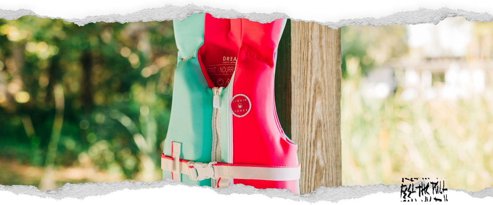 Side view of pink and mint infant CGA vest with Liquid Force patch, hanging from a wooden post.