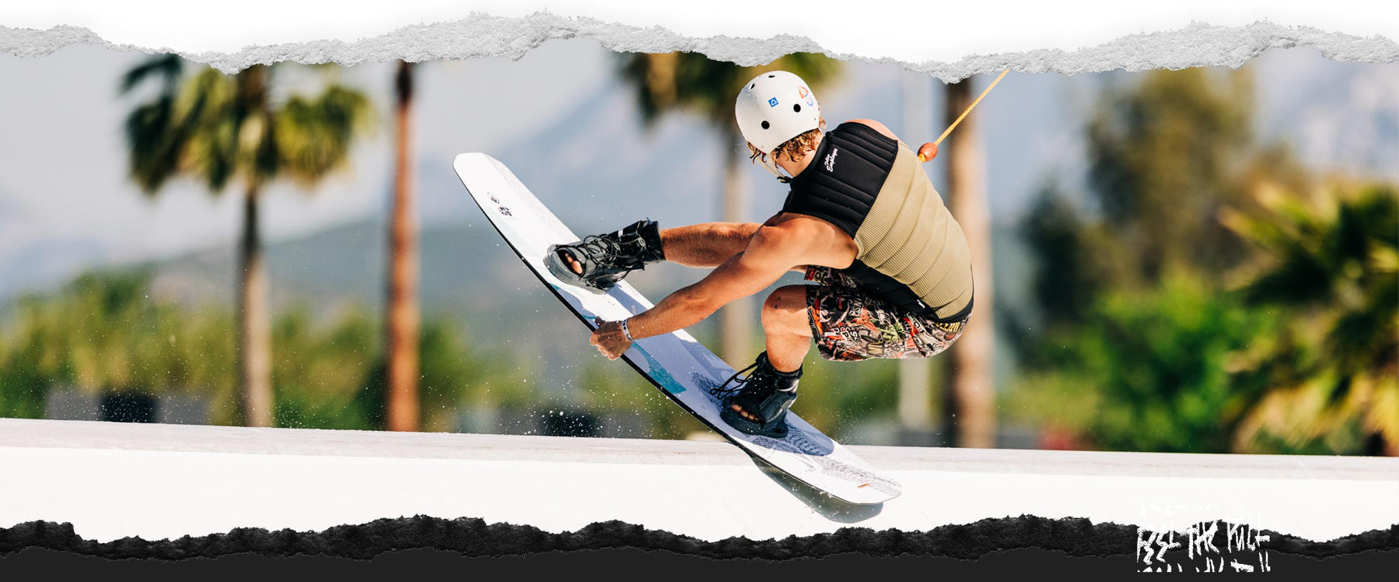 Wakeboarder in vest and helmet grabs the Liquid Force FLX wakeboard mid-air on a rail.