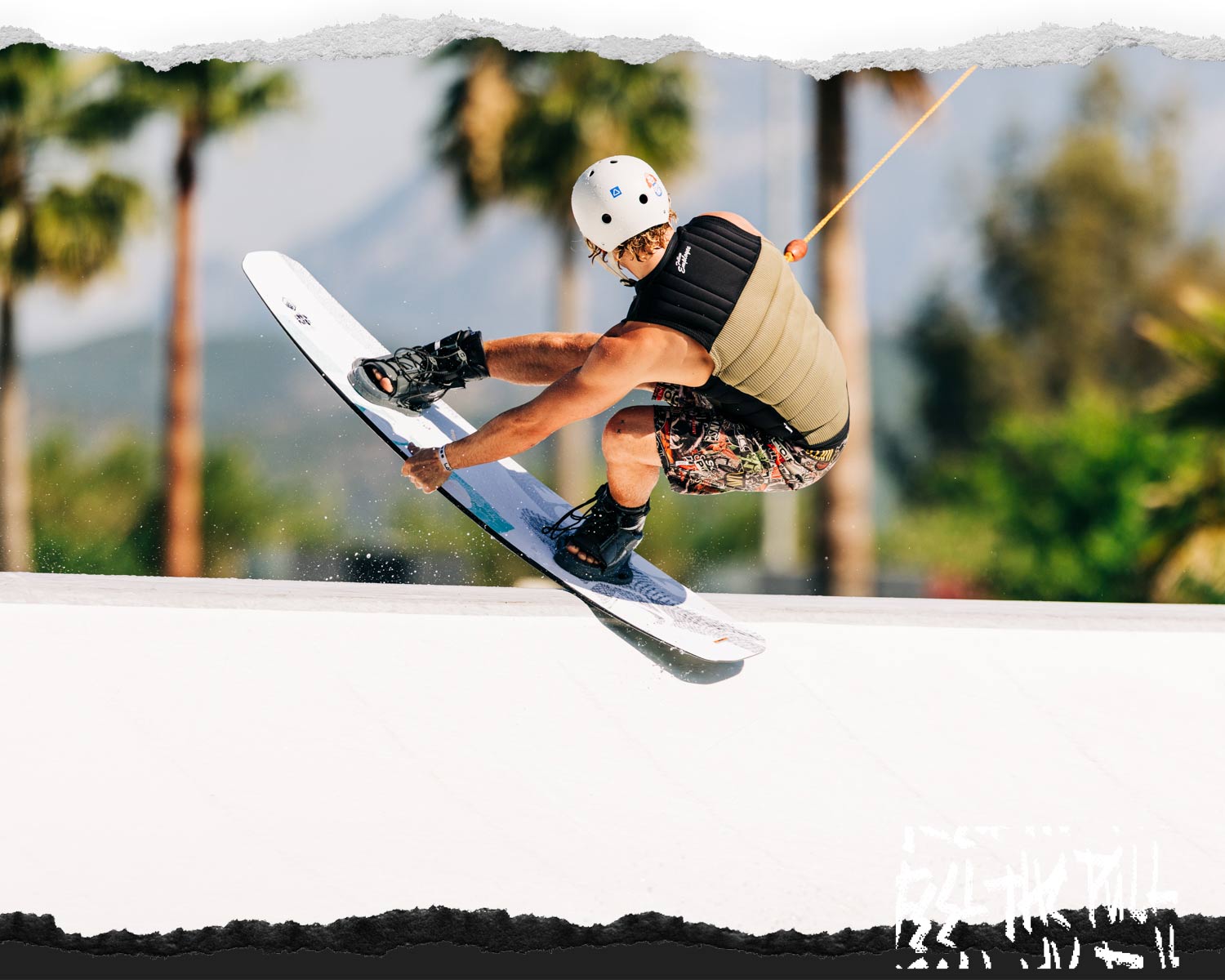 Wakeboarder in vest and helmet grabs the Liquid Force FLX wakeboard mid-air on a rail.