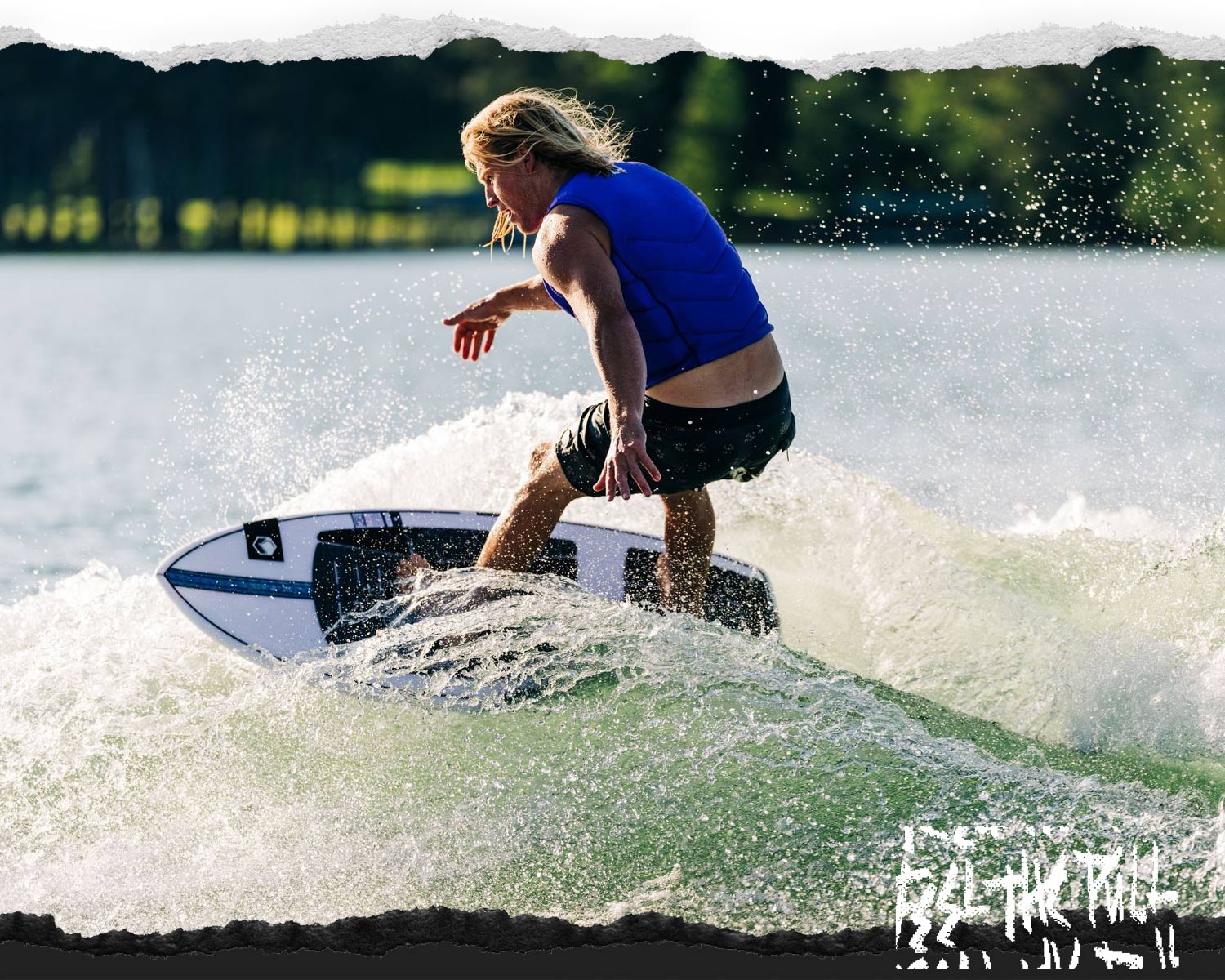Rider in blue vest bottom turning on a white and blue wakesurf board on a lake.