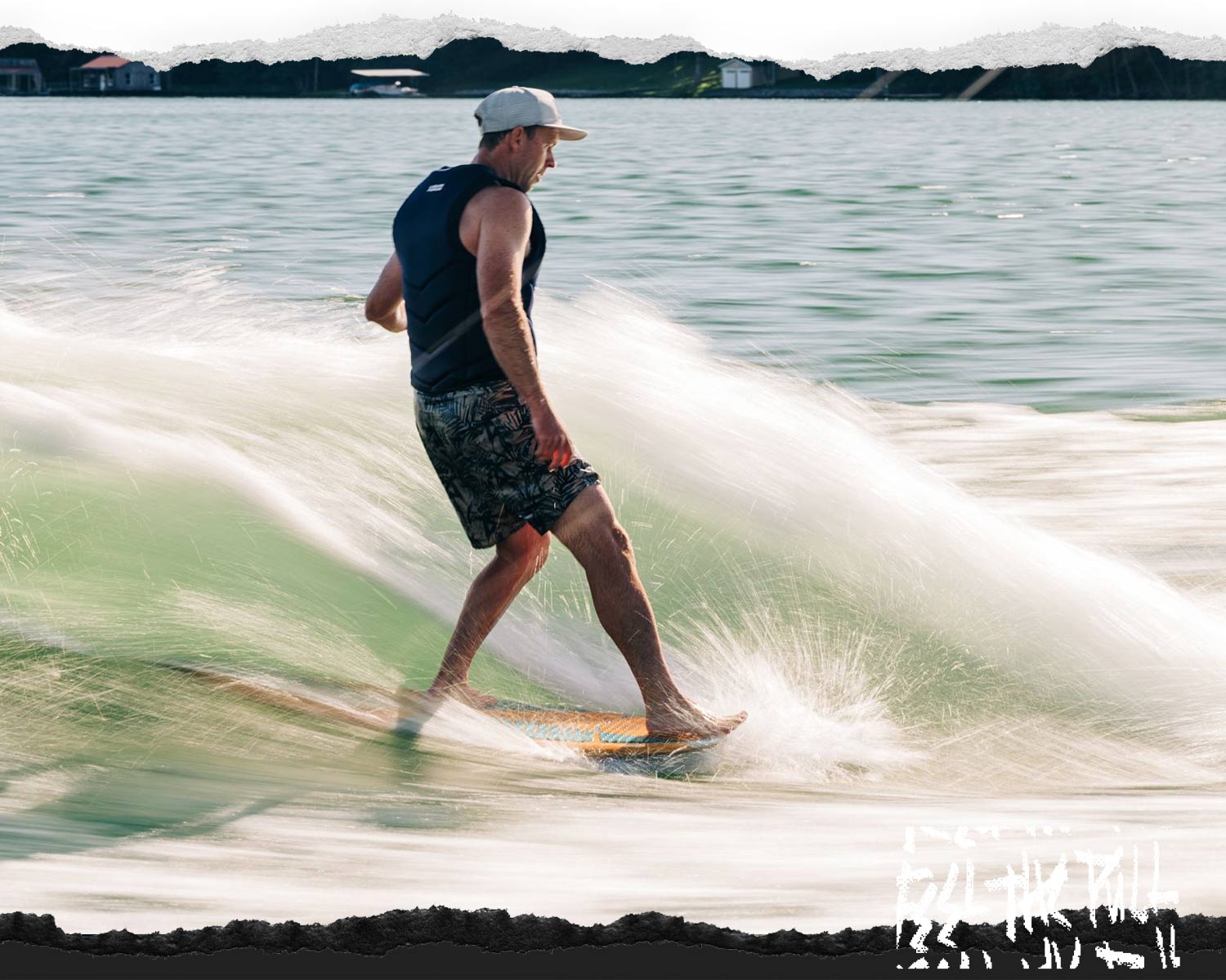 Rider in blue vest carving on a wave on a light wood wakesurf board with green water spray.