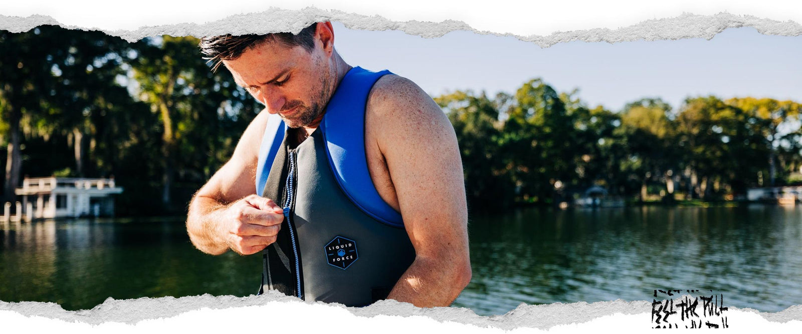 Man zips up blue and black Hinge CGA vest while standing on dock in front of water.