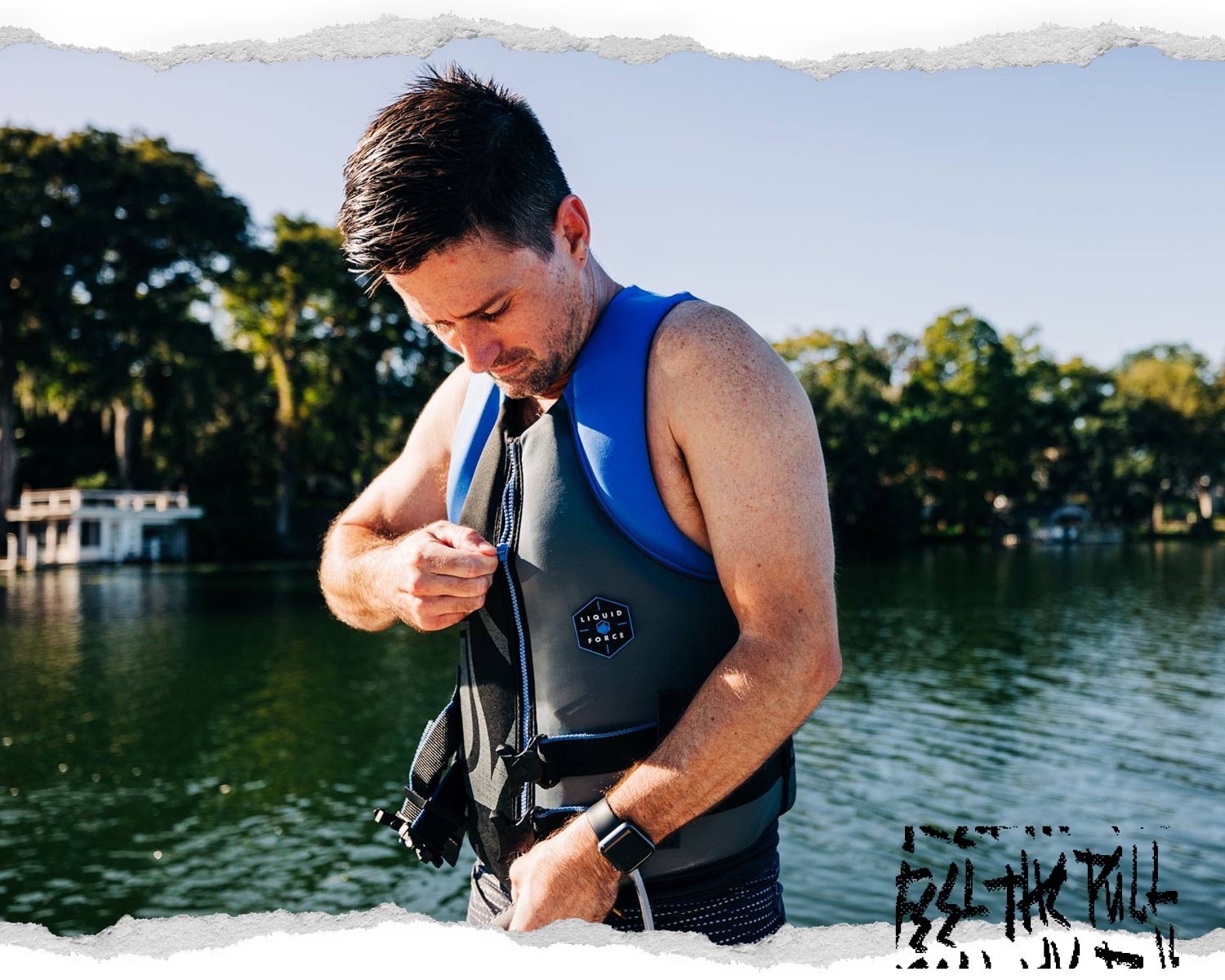 Man zips up blue and black Hinge CGA vest while standing on dock in front of water.