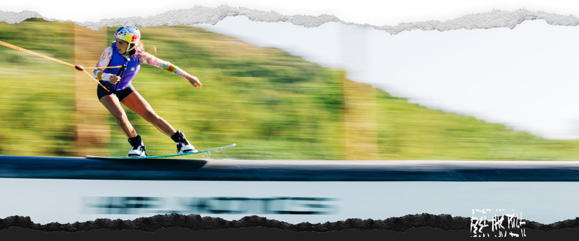 Wakeboarder in purple vest and Red Bull helmet slides a rail on a Liquid Force board.