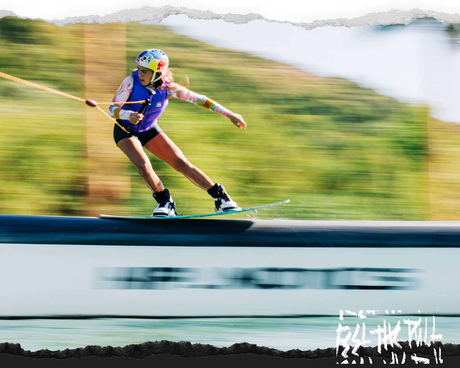Wakeboarder in purple vest and Red Bull helmet slides a rail on a Liquid Force board.