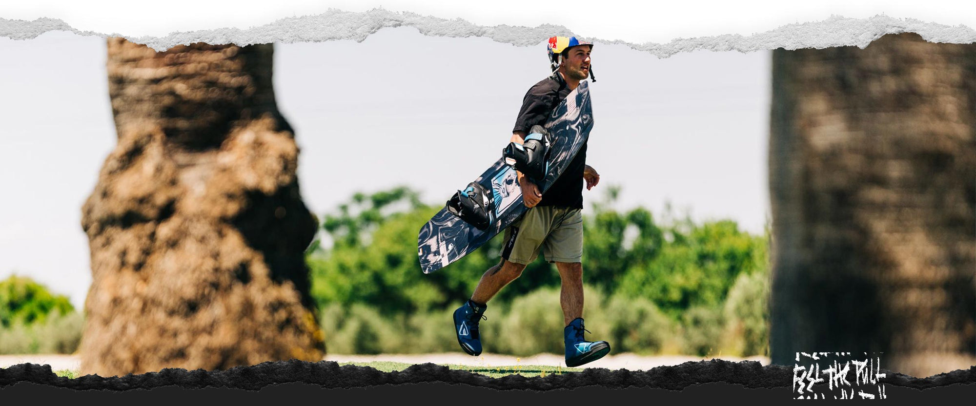 Wakeboarder on grass carrying black board with blue boots.