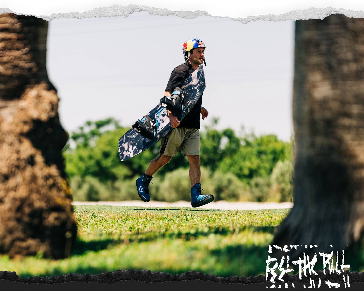Wakeboarder on grass carrying black board with blue boots.