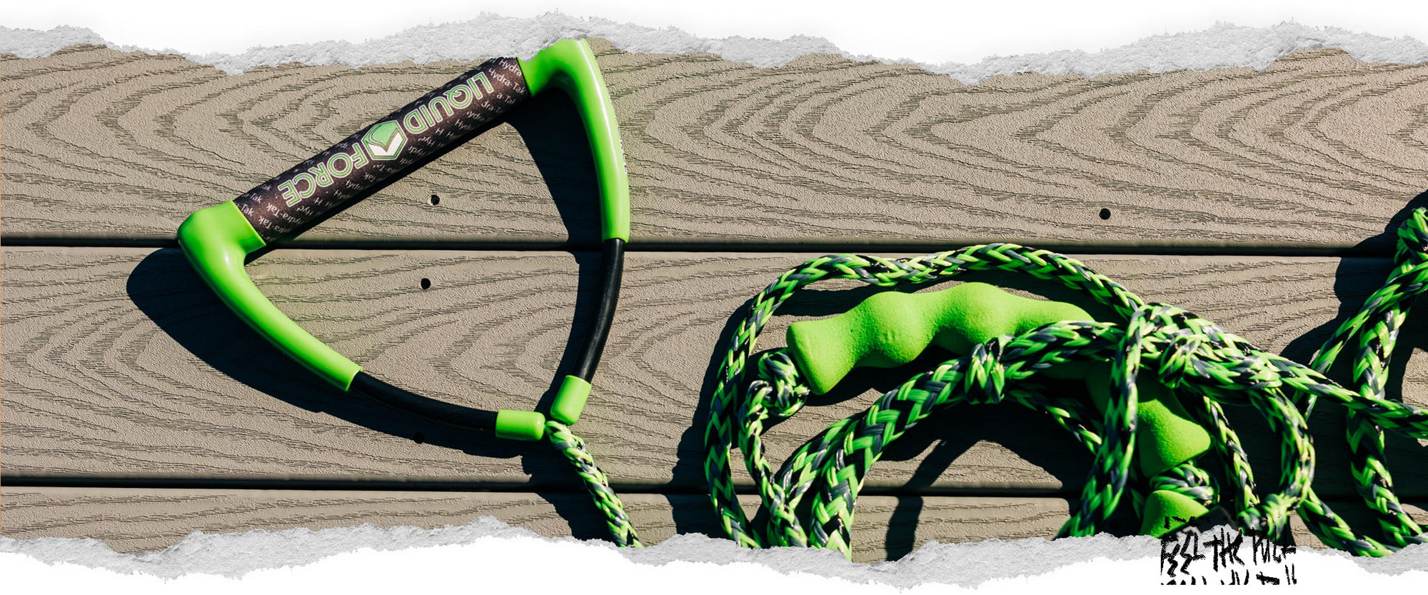 Green Liquid Force handle and rope resting on wood deck in bright sun.