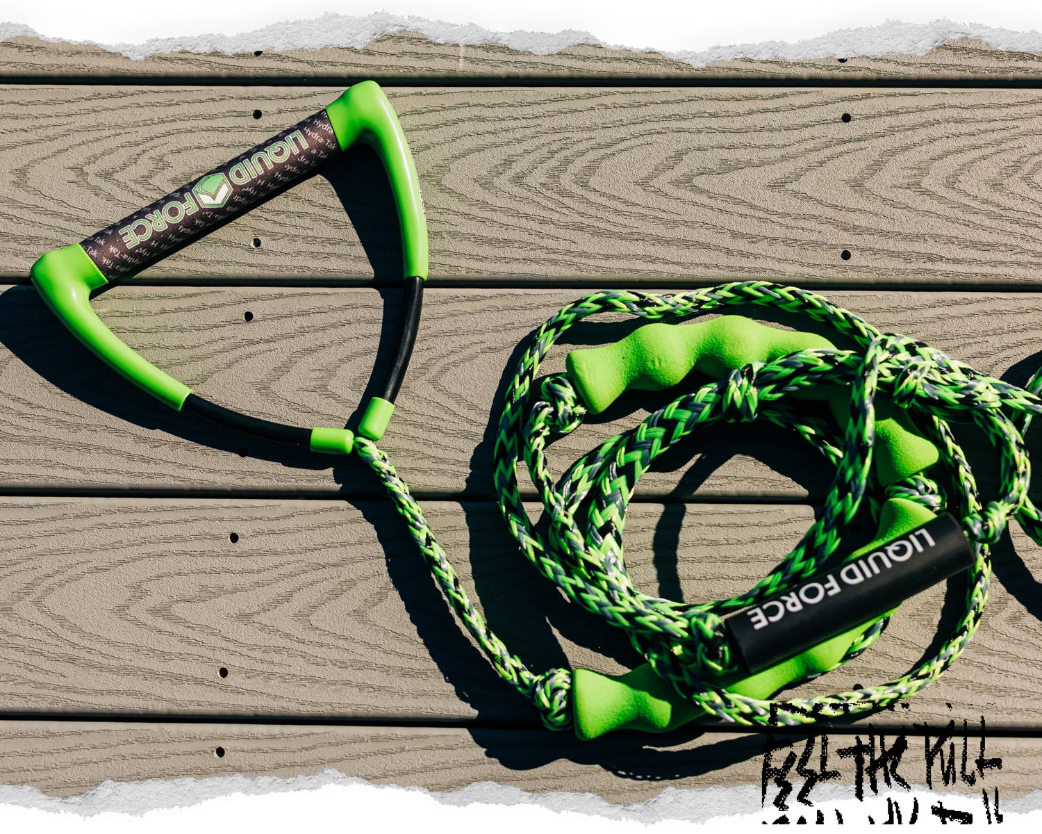 Green Liquid Force handle and rope resting on wood deck in bright sun.