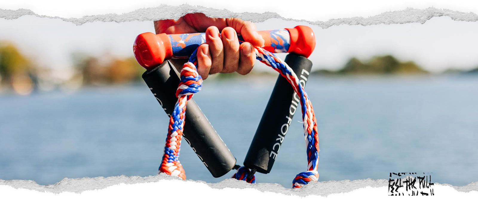 Hand holding red, white, and blue Liquid Force surf rope above water.