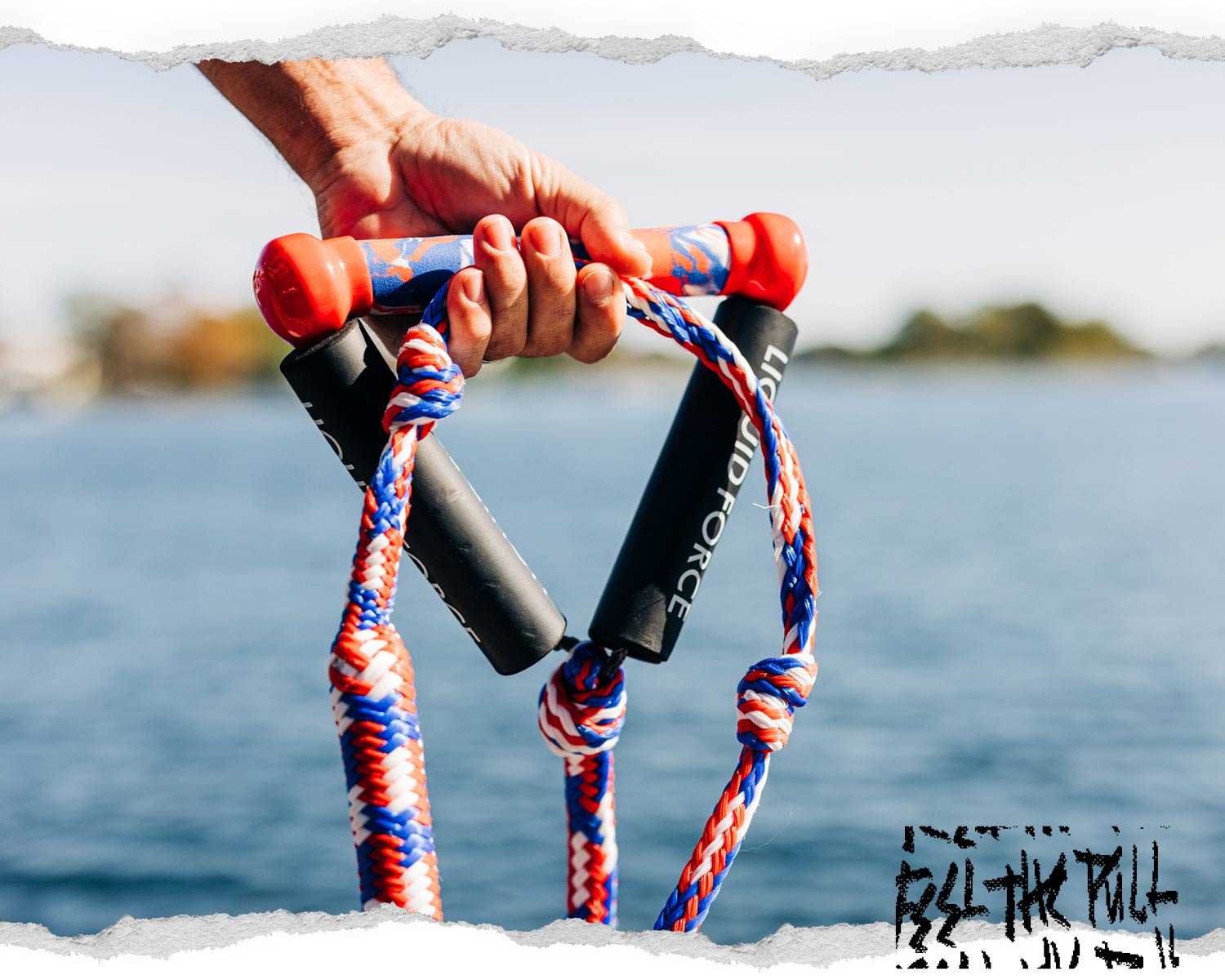 Hand holding red, white, and blue Liquid Force surf rope above water.