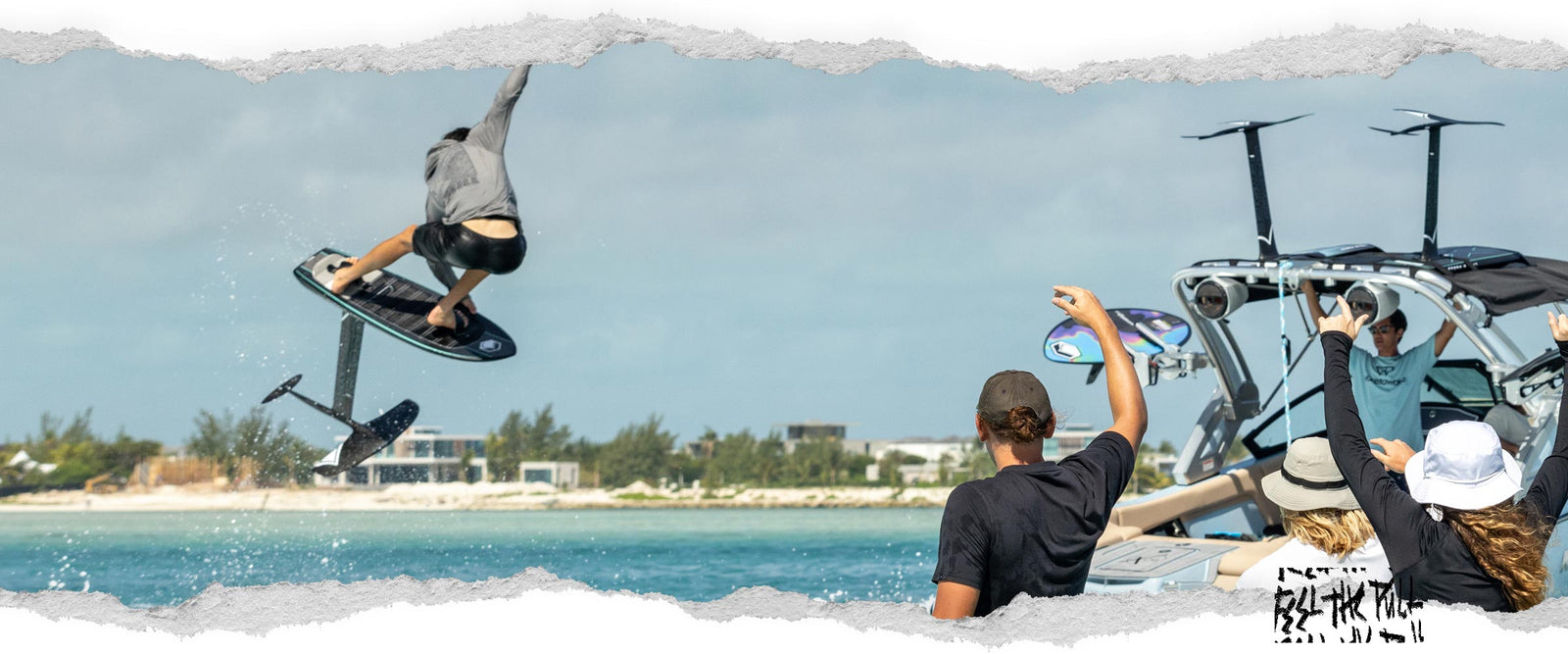 Rider launches on foil board as friends cheer from boat in turquoise water.