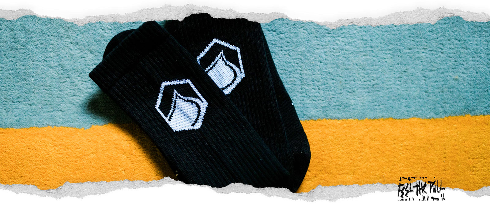 Pair of black socks with white logo on a textured teal and yellow surface.