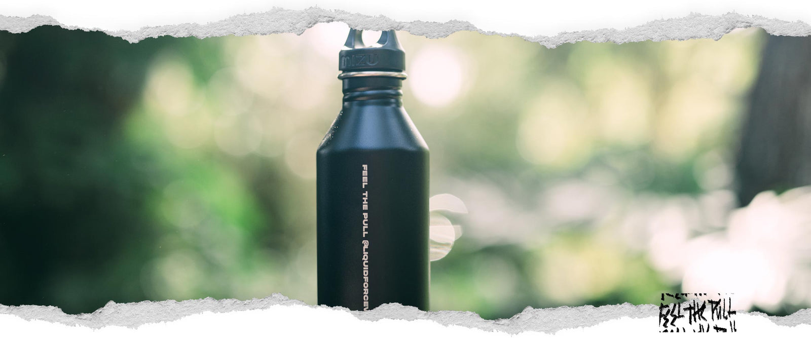 A black metal water bottle with the text "FEEL THE PULL" and blurred greenery in the background.