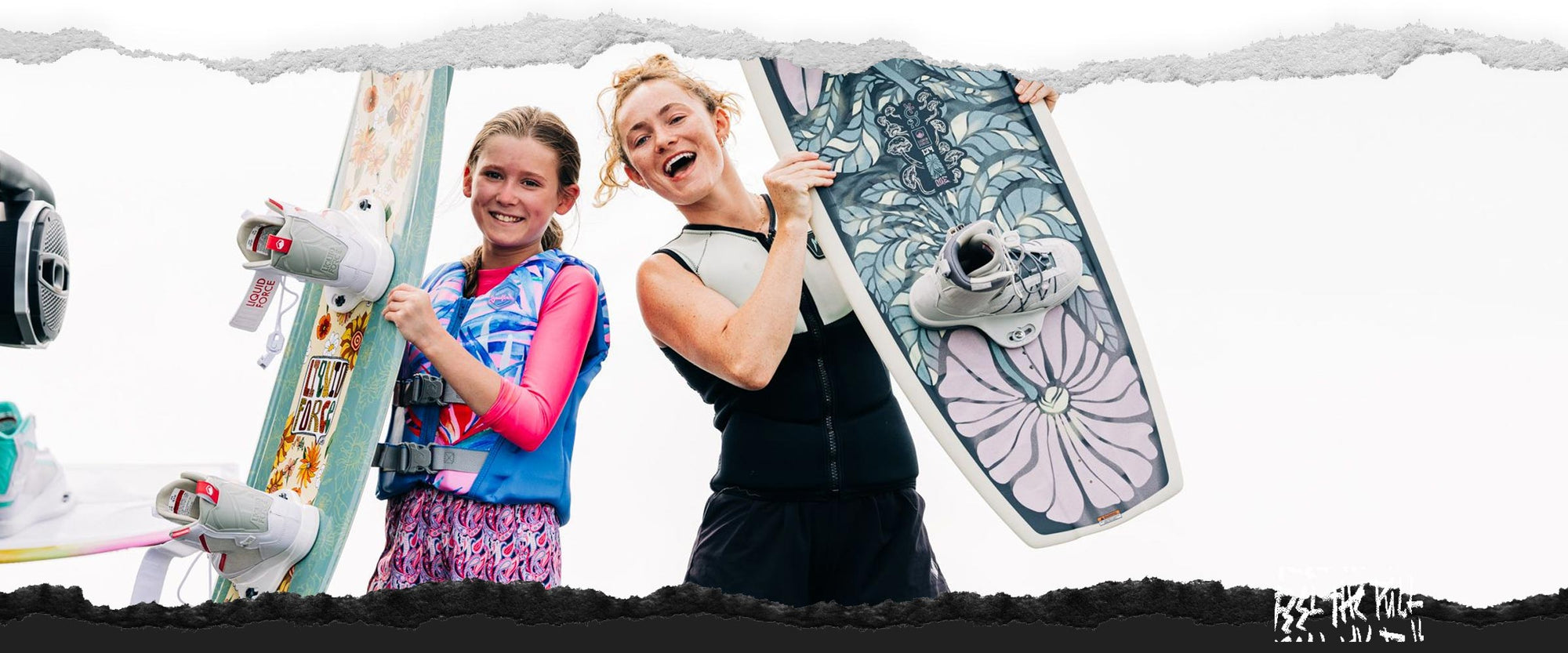 Two girls smiling and holding floral Liquid Force wakeboards.