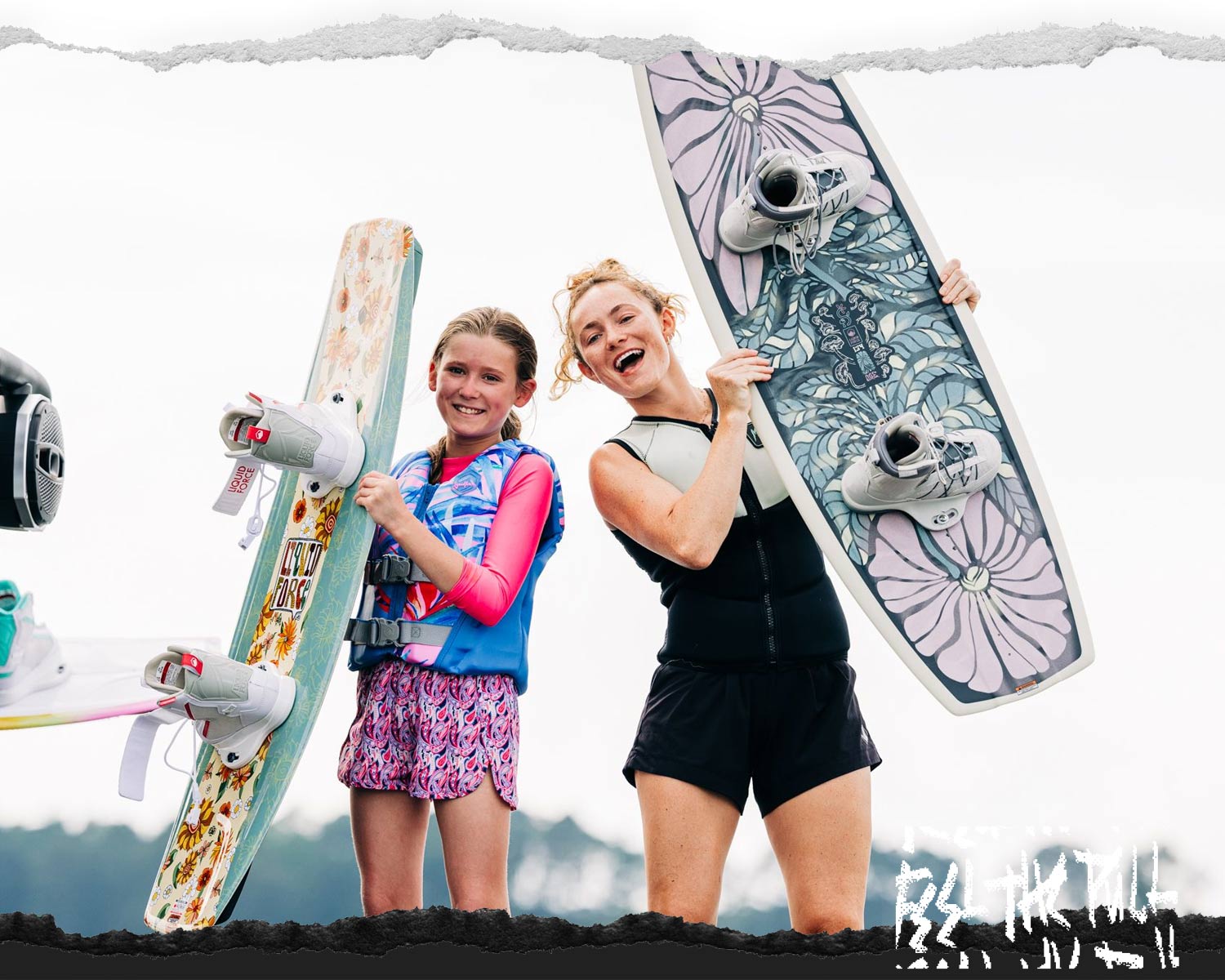 Two girls smiling and holding floral Liquid Force wakeboards.