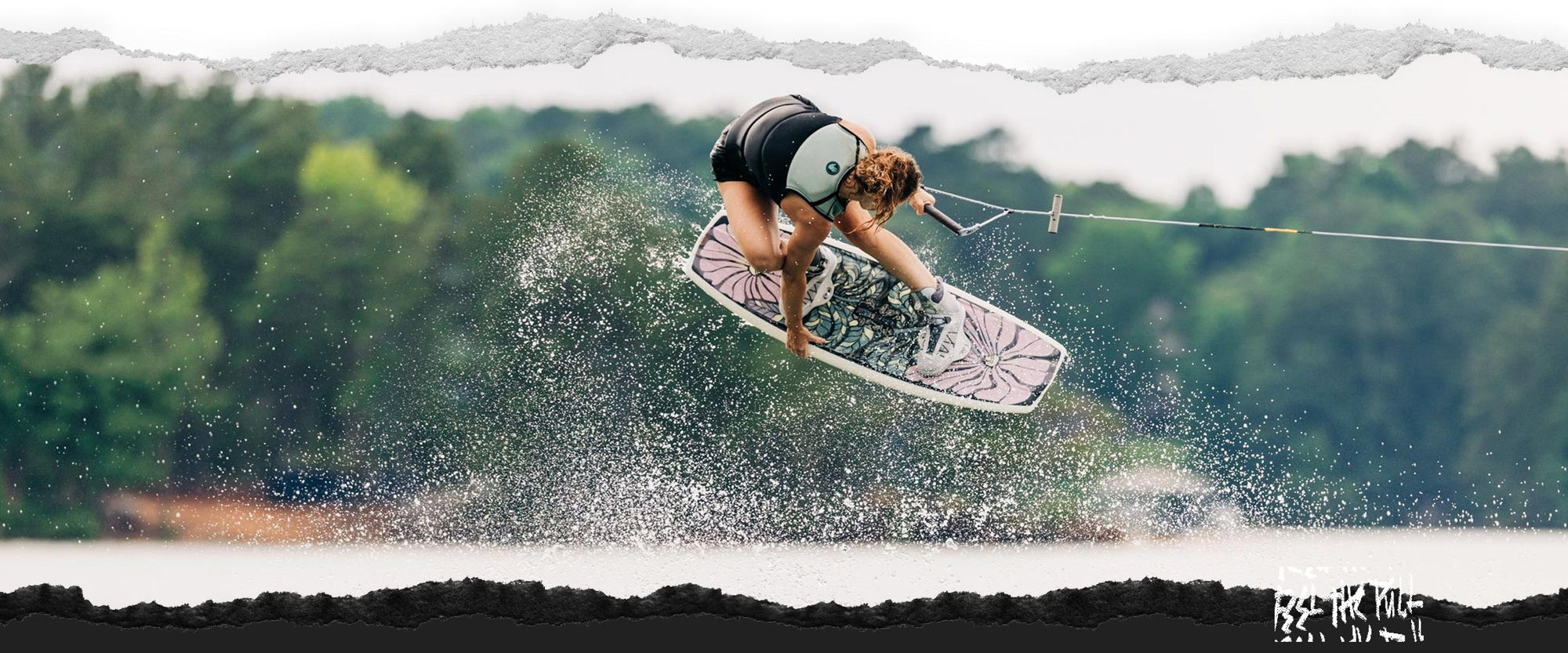 Wakeboarder in air above lake holding floral-patterned board.