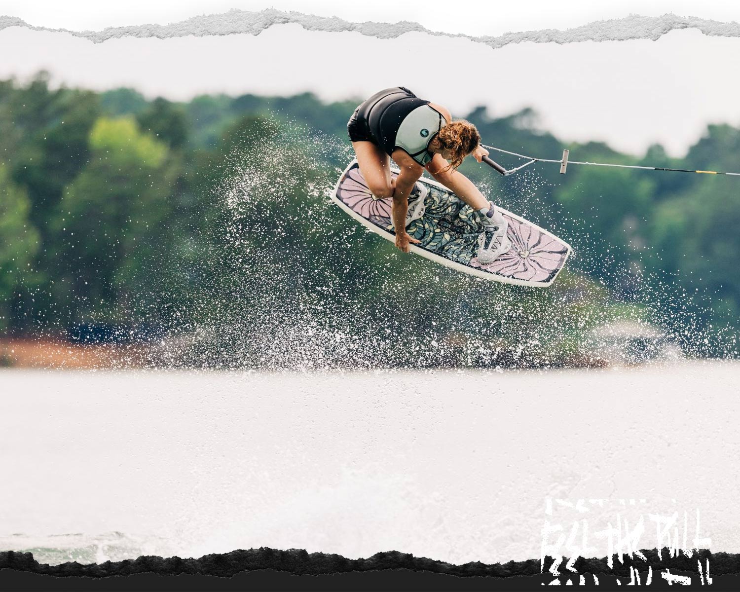 Wakeboarder in air above lake holding floral-patterned board.